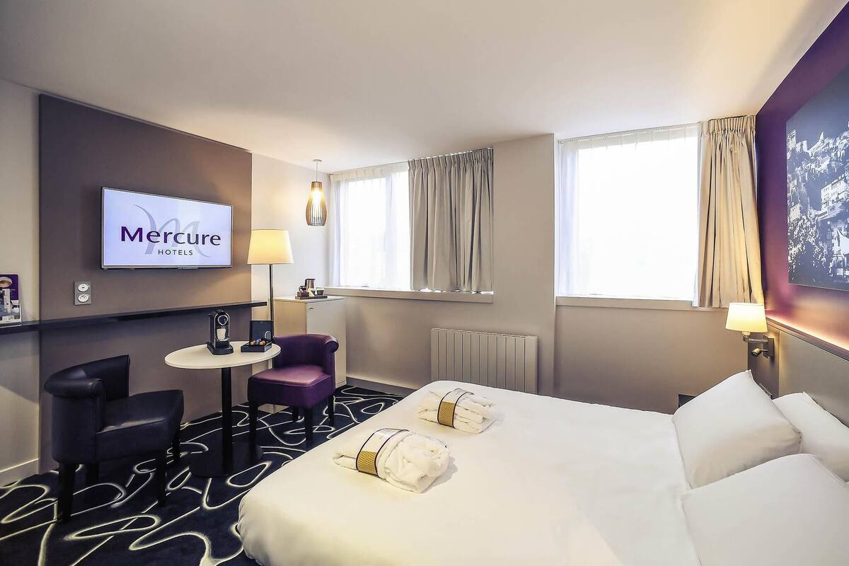 A hotel room with a bed, a desk, a chair, a TV, and a window with curtains.