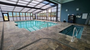 Une piscine intérieure avec des parois en verre transparent, un sol carrelé et une petite piscine attenante.