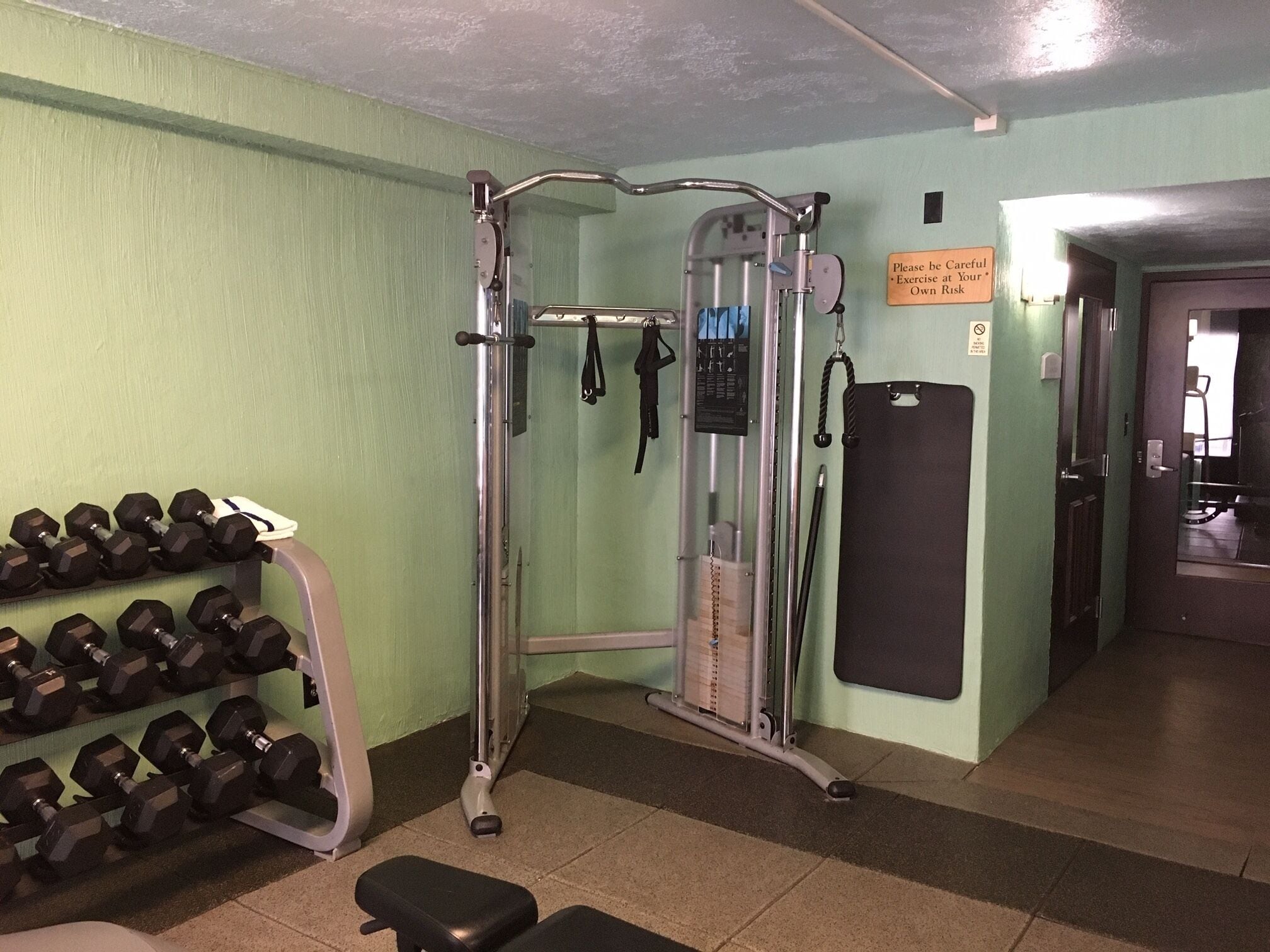 A gym with exercise equipment, a wall-mounted dumbbell rack, and a sign advising caution.