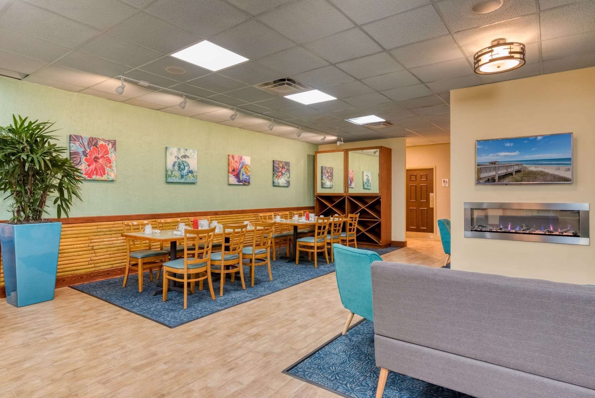Un espace repas avec des tables et des chaises en bois, un mur d’accent bleu et des œuvres d’art.