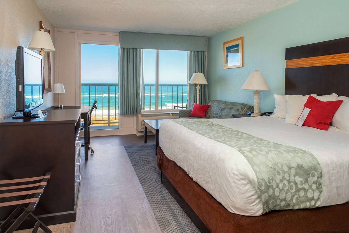 Een hotelkamer met een bed, bureau en stoel, een televisie en uitzicht op de oceaan.