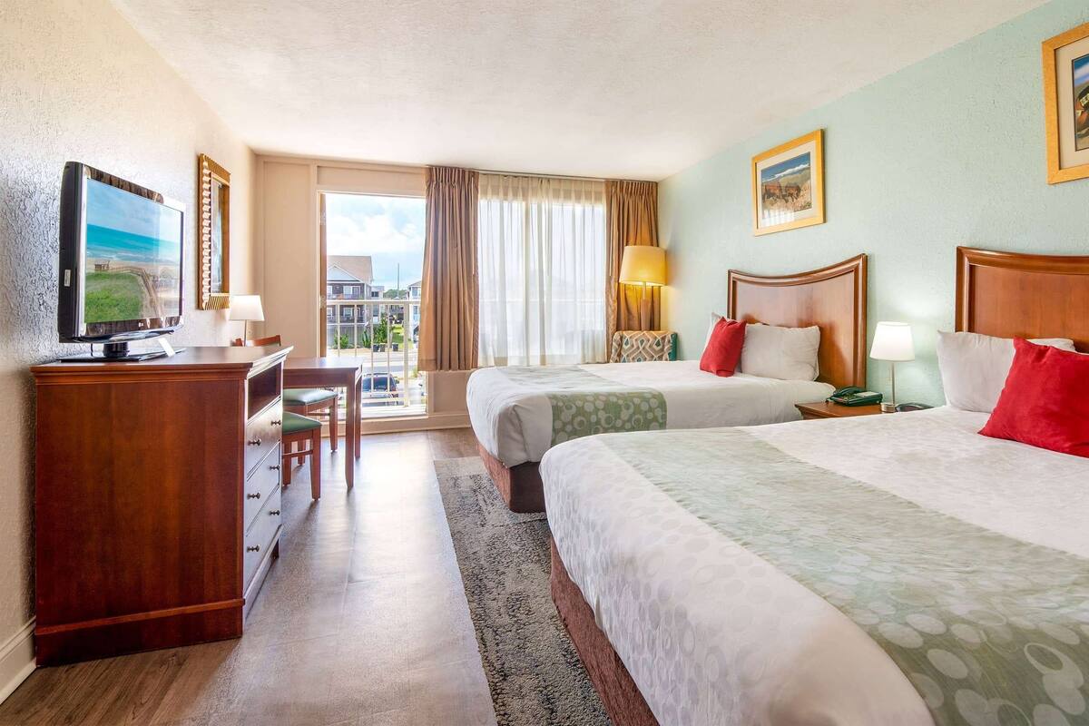 Een hotelkamer met twee bedden, een bureau, een televisie en uitzicht op de stad.