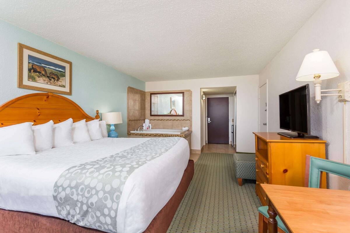 Een hotelkamer met een groot bed, een bureau met een televisie, een badkamer met een wastafel en spiegel, en een deur die leidt naar een andere kamer.