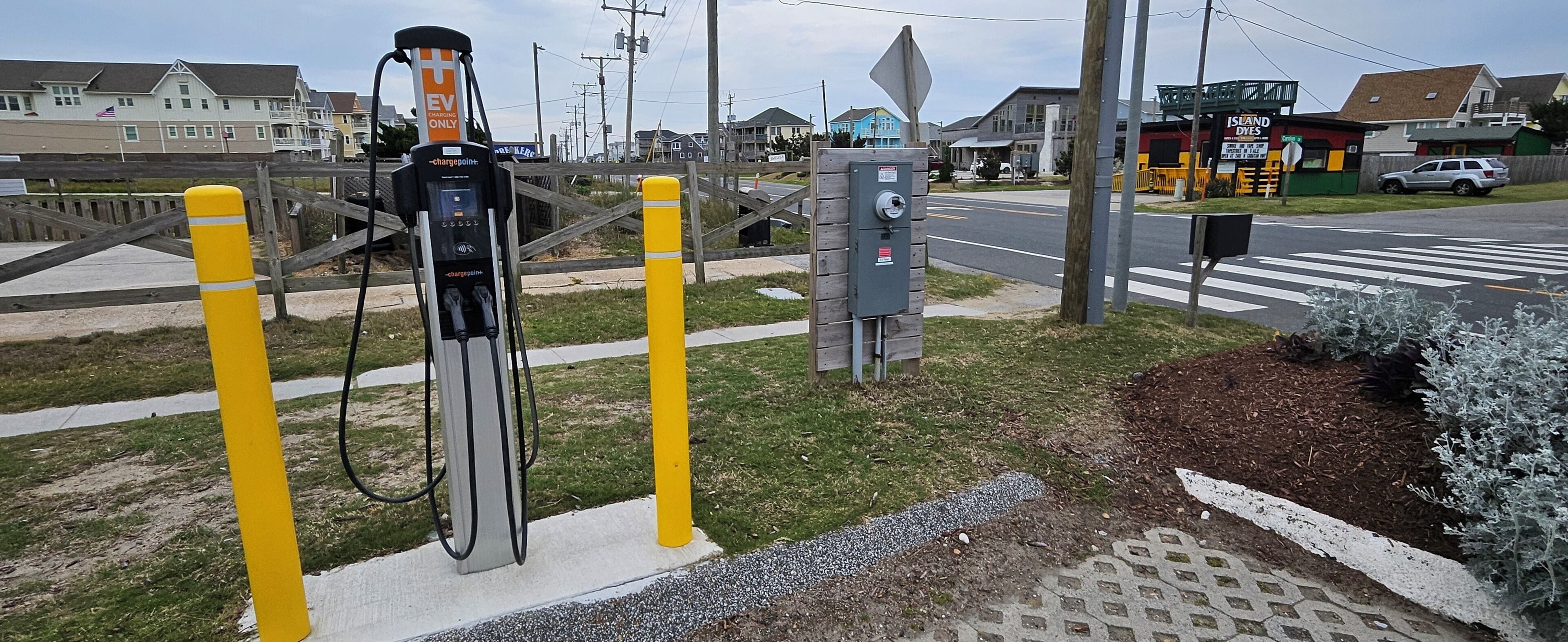 An electric vehicle charging station with a wooden fence and a street view in the background.