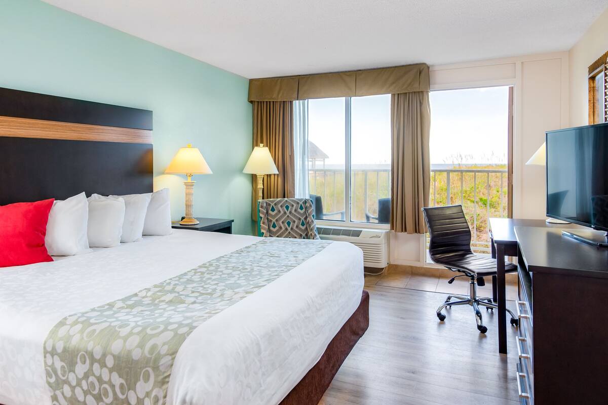 Een hotelkamer met een bed, een bureau met televisie, een stoel, een lamp en een raam met gordijnen.