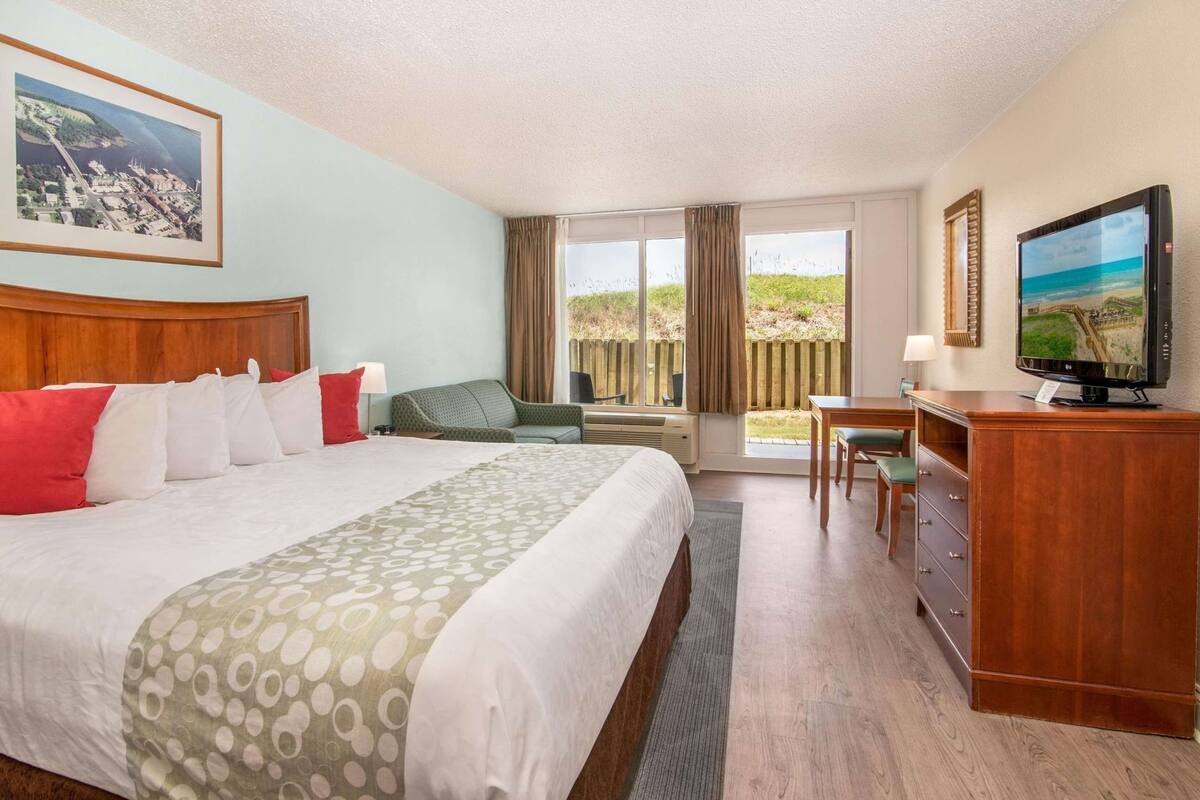 Een hotelkamer met een groot bed, een bureau met stoel, een televisie en een raam met uitzicht op het strand.