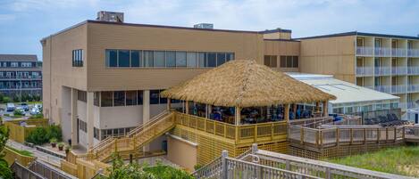 A hotel with a thatched-roof outdoor seating area, a pool, and a wooden deck.