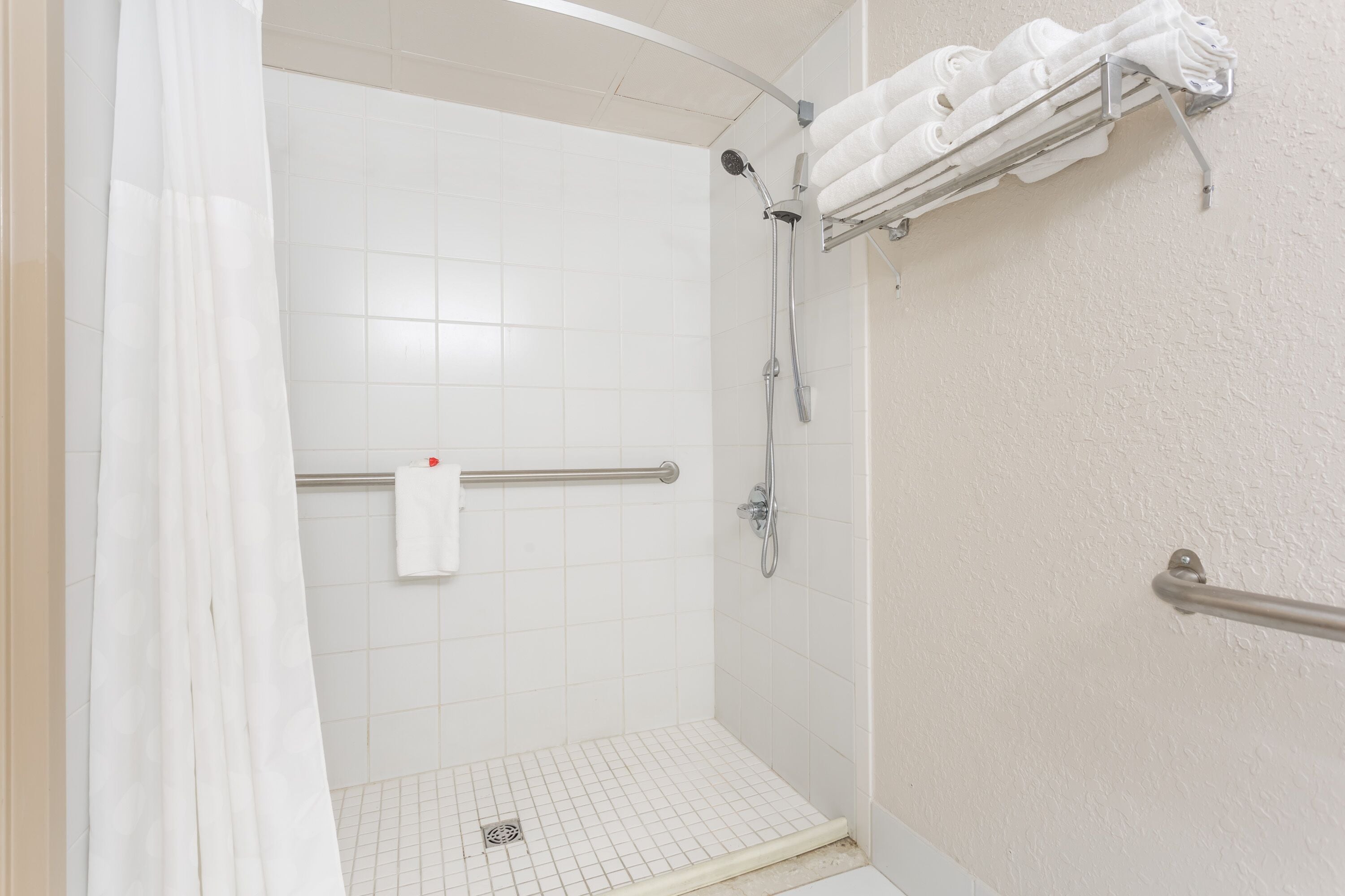 A shower with a glass door, a towel rack with folded towels, and a handrail.