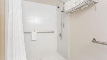 Een douche met een glazen deur, een handdoekhouder met opgevouwen handdoeken en een handgreep.