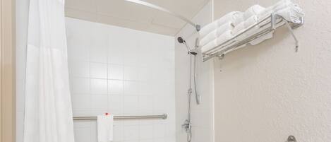 A shower with a glass door, a towel rack with folded towels, and a handrail.
