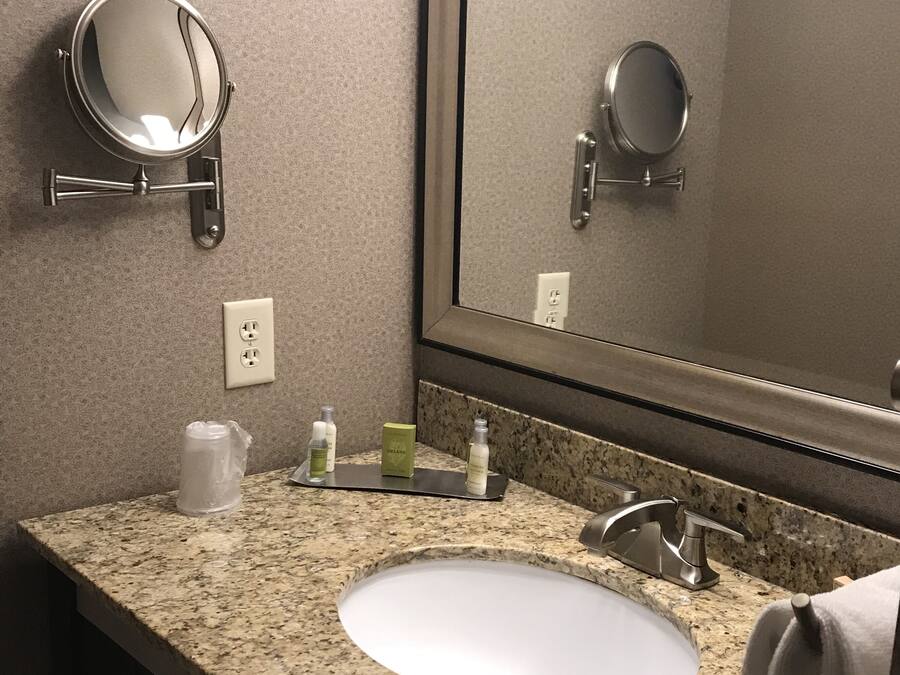 A bathroom with a granite countertop, a white sink, a mirror, and a towel hanging on the wall.