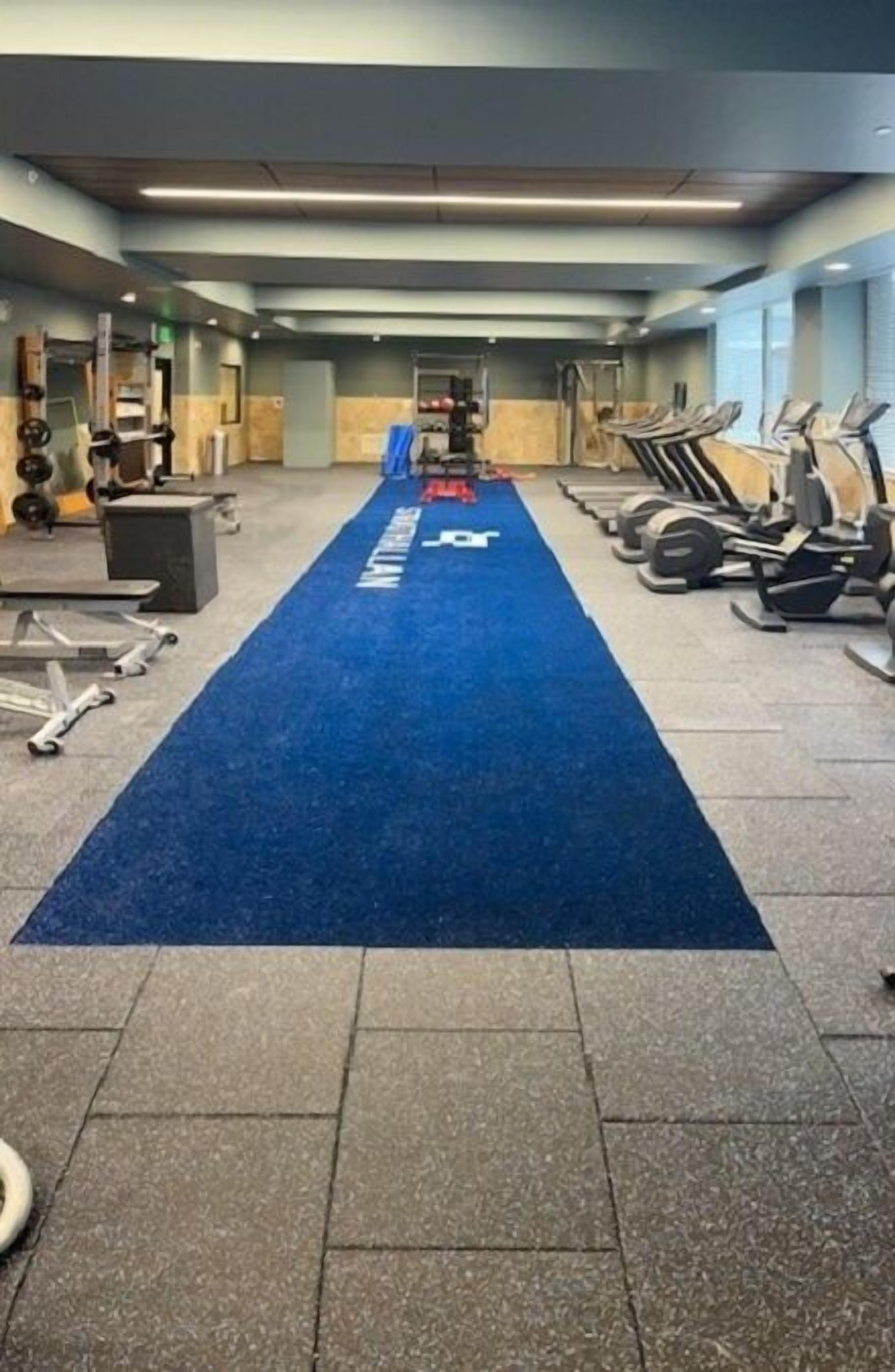 Ein Fitnessraum mit Trainingsgeräten, einem blauen Teppich und einer Gewichtbank.