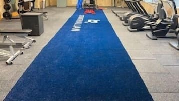 Ein Fitnessraum mit Trainingsgeräten, einem blauen Teppich und einer Gewichtbank.