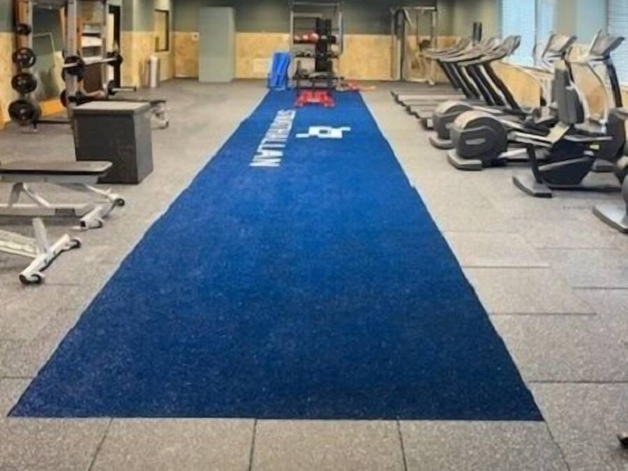 Ein Fitnessraum mit Trainingsgeräten, einem blauen Teppich und einer Gewichtbank.