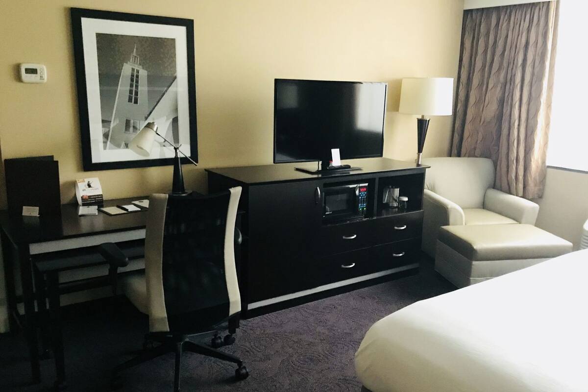 Una camera d'albergo con un letto, una scrivania con un computer, una sedia, una televisione e una lampada.