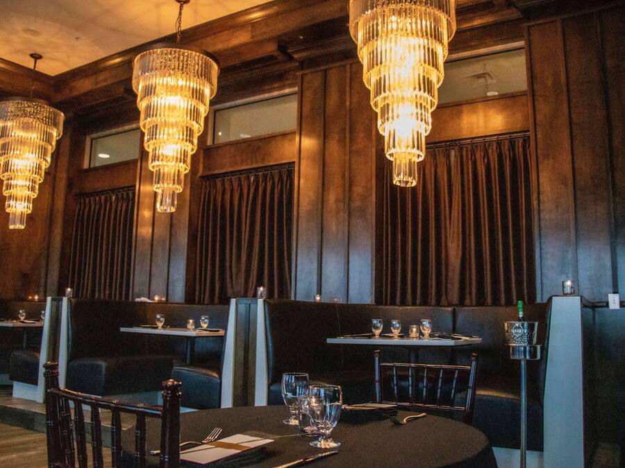 A restaurant with multiple tables, each set with cutlery and glasses, and three large chandeliers hanging from the ceiling.