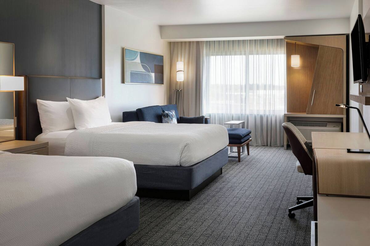 A hotel room with a large bed, a desk, a chair, and a TV.