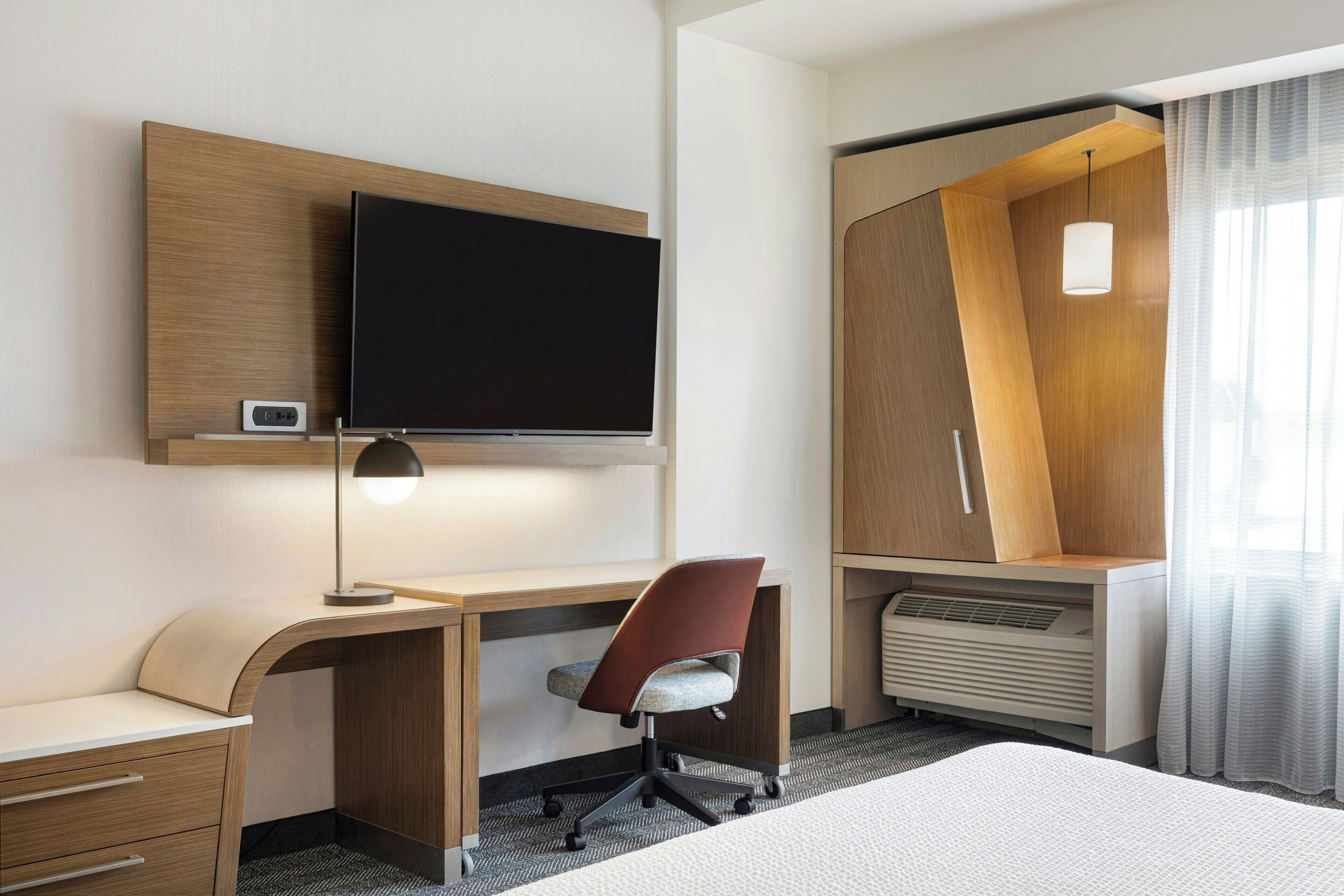 Quarto de hotel com cama, mesa, cadeira, televisão e guarda-roupa.