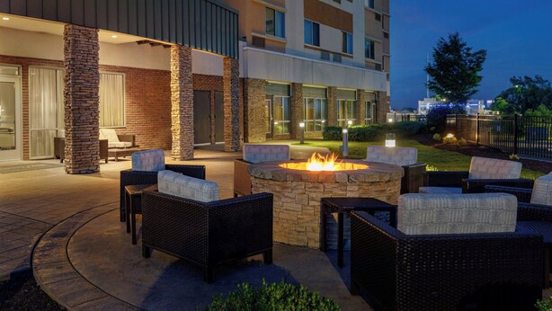 Un patio al aire libre con mobiliario de mimbre, un hogar de piedra y un edificio al fondo.