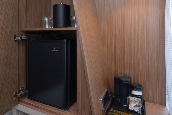 Un refrigerador negro compacto con una cafetera y un recipiente para leche sobre un estante de madera.
