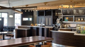 Un bar moderno con mobiliario de madera, una barra con menú y una zona de estar con mesas y sillas.