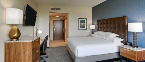 Una habitación de hotel con una cama, un escritorio con lámpara, una silla y un televisor en la pared.