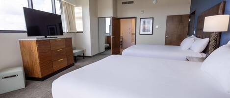 A hotel room with two beds, a TV, a wooden dresser, and a large window.