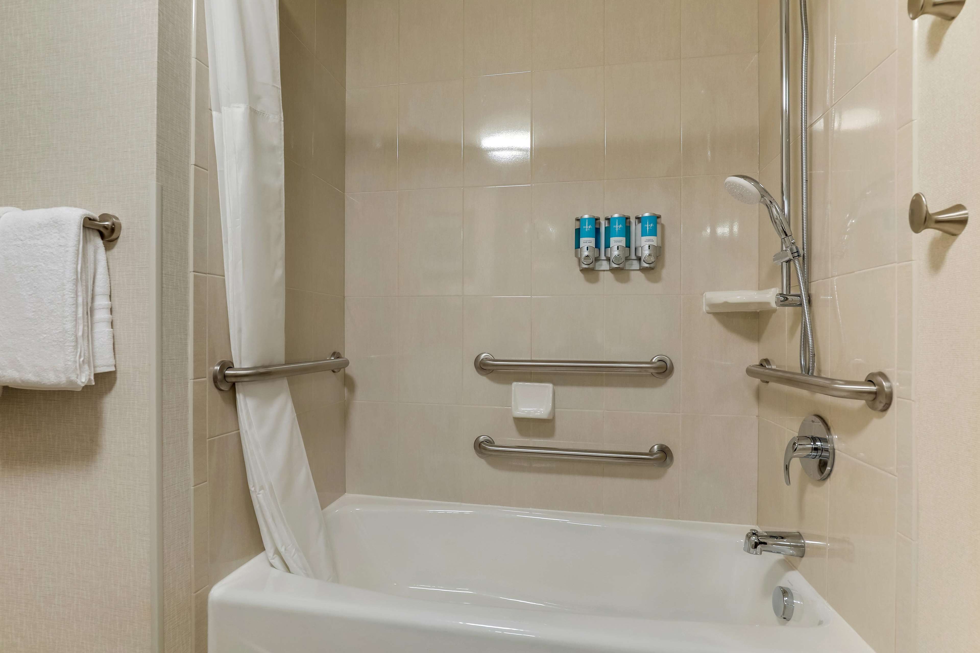 A bathroom with a bathtub, grab bars, a showerhead, and a towel rack.
