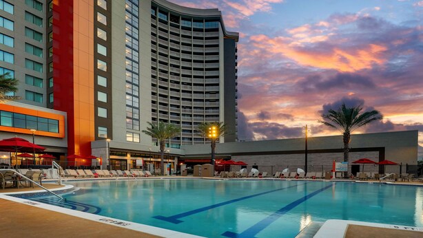 A hotel pool area with lounge chairs and umbrellas, surrounded by tall buildings and a sunset sky. - Drury Plaza Hotel Orlando - Disney Springs Area (Lake Buena Vista)