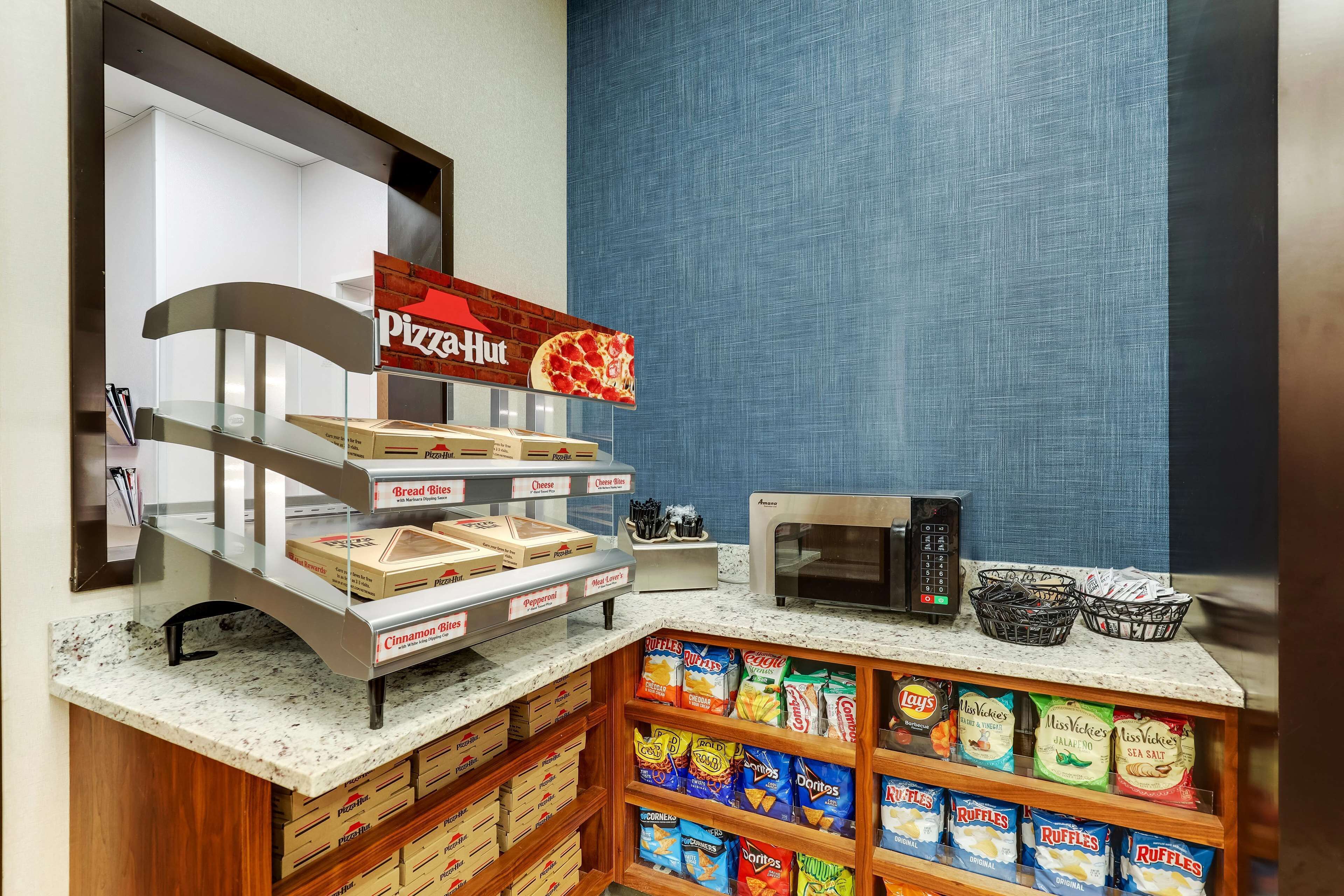 A self-serve breakfast area with pizza, bread, and cereal options, a microwave, and various snack bags.