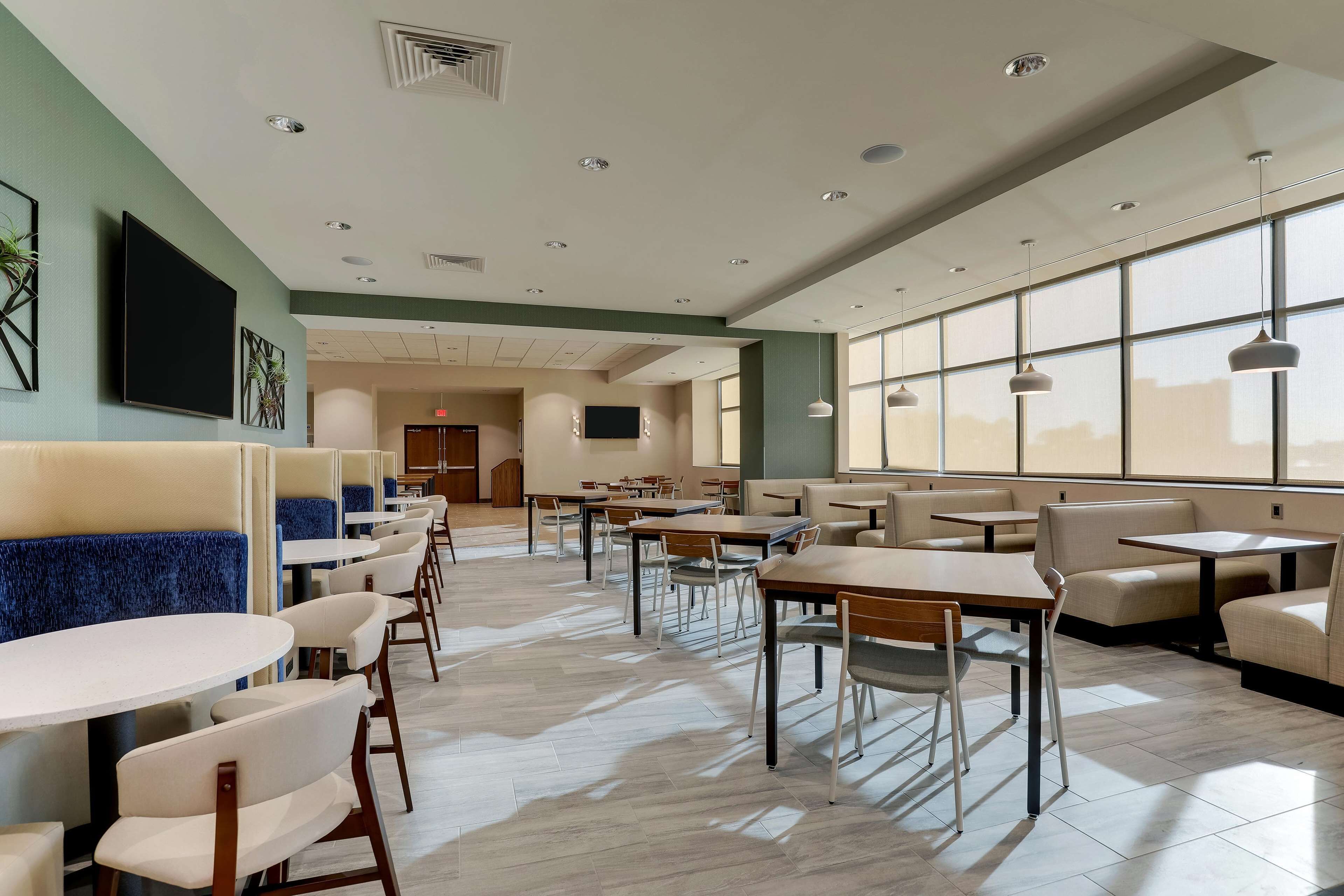 Un espace repas moderne avec des banquettes et des tables, de grandes fenêtres et un éclairage encastré.