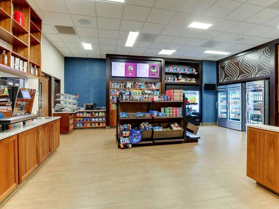 Een schone, goed verlichte winkel met houten schappen vol met diverse producten, een koelvitrine en een digitaal menu.