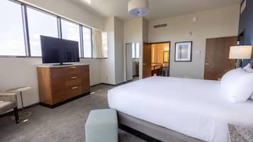 Habitación de hotel con una cama grande, televisión, escritorio y vista al cielo a través de las ventanas.