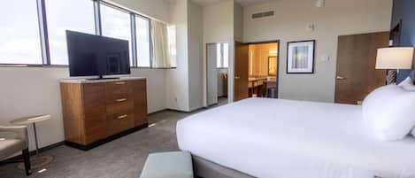 A hotel room with a large bed, a television, a desk, and a view of the sky through the windows.