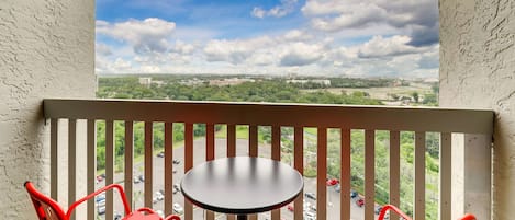 A balcony with a table and chairs, overlooking a parking lot and a cityscape.