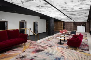 A modern hotel lobby with a red sofa, a small table, and a reception desk.