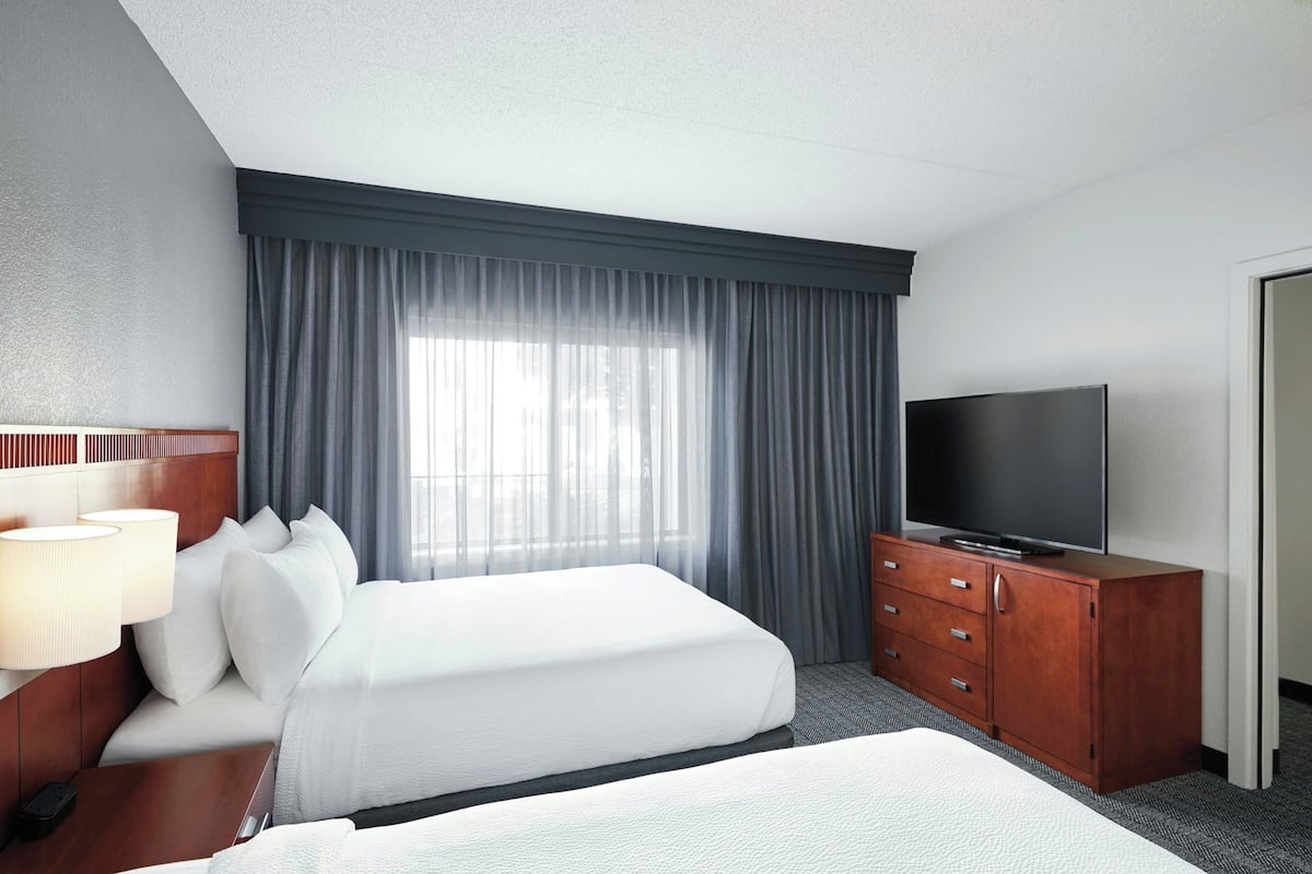 A hotel room with a large bed, a TV on a wooden cabinet, and a window with curtains.