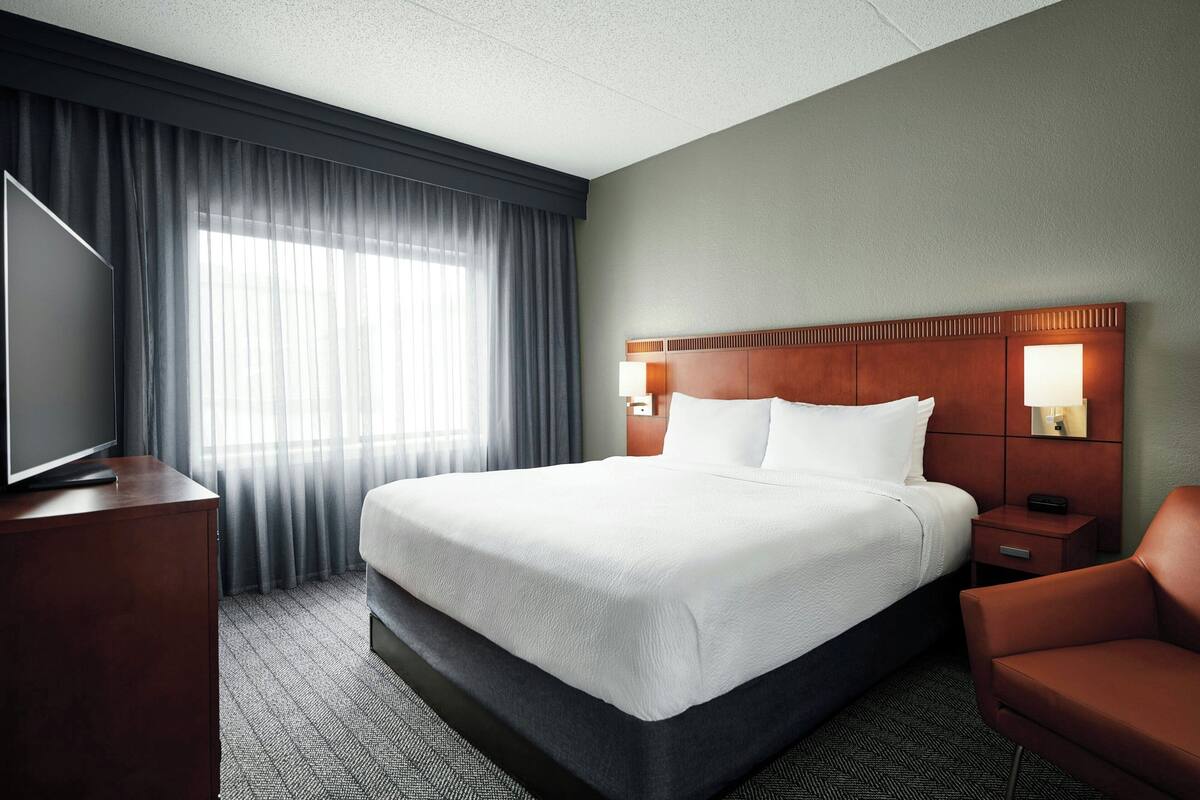 A hotel room with a large bed, a TV on a wooden cabinet, a desk, and a chair.