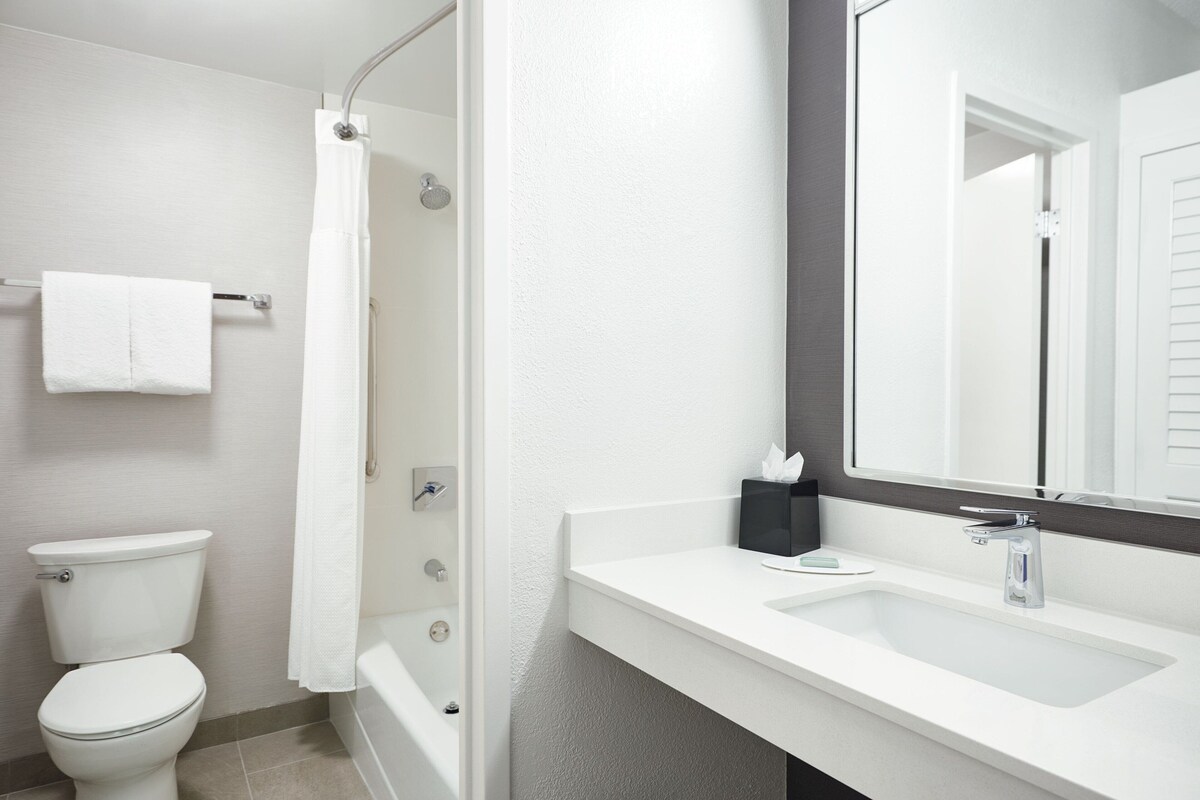 A modern bathroom with a white toilet, a bathtub, and a sink with a mirror above it.