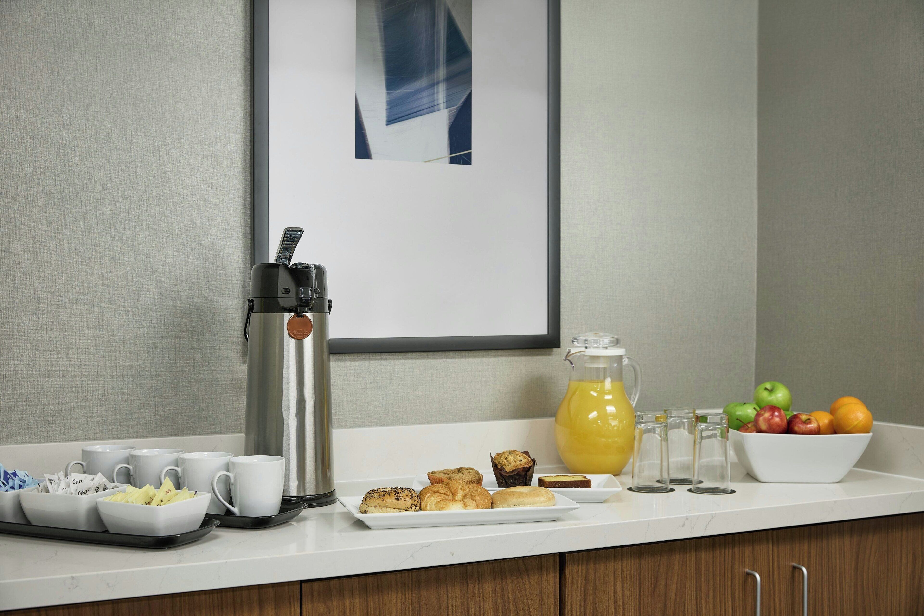 Un buffet de petit-déjeuner avec du café et du thé, des viennoiseries et un saladier de fruits, le tout disposé sur le comptoir d’un hôtel.