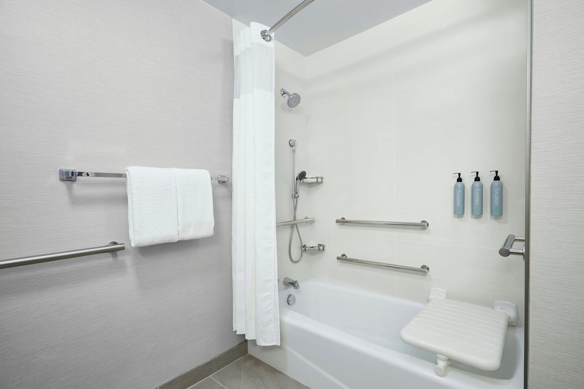 A modern bathroom with a walk-in shower, grab bars, a white bathtub, and a towel rack.