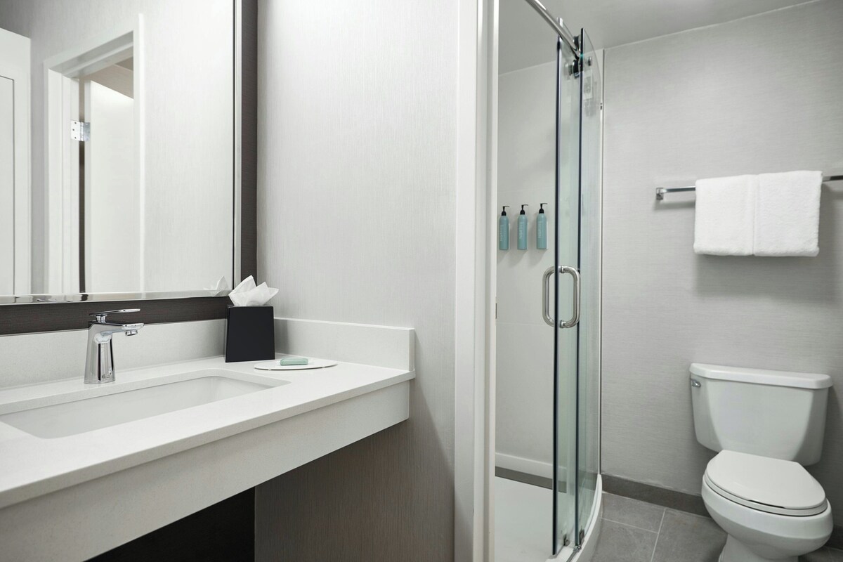 A modern bathroom with a glass shower enclosure, a white toilet, and a sink with a mirror.