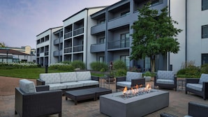 An outdoor seating area with wicker furniture, a fire pit, and a modern building in the background. - Courtyard by Marriott St Louis Westport Plaza (Maryland Heights)