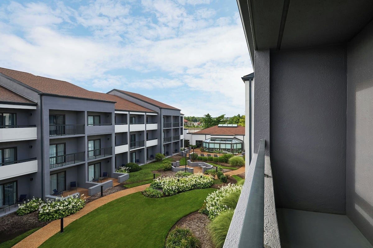 A modern multi-story building with balconies, a courtyard with greenery, and a clear sky.
