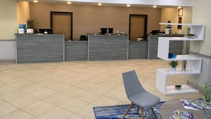 A reception area with a reception desk, two doors, a blue chair, a round table with brochures, and a small shelf with plants. - Clarion Hotel Fort Mill Near Amusement Park (Fort Mill)