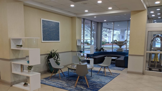 A modern waiting area with a blue rug, white chairs, a sofa, and a large window offering a view of the outside. - Clarion Hotel Fort Mill Near Amusement Park (Fort Mill)