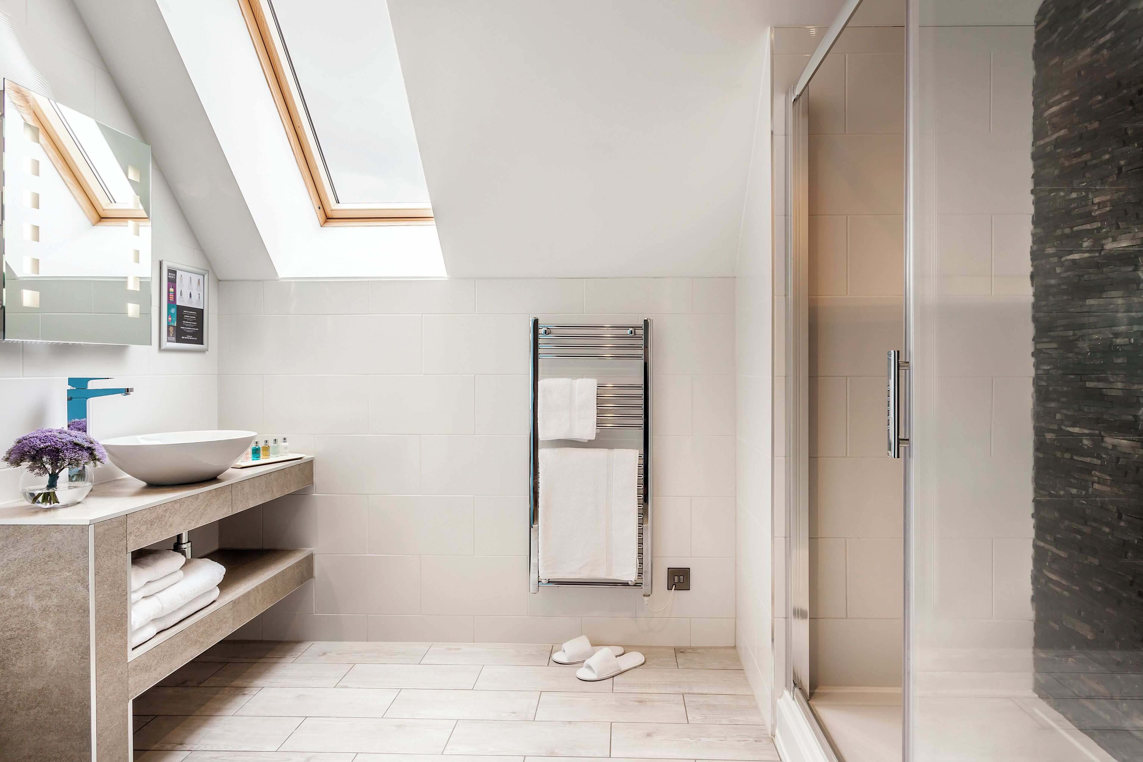 A modern bathroom with a skylight, a large sink, a towel rack, and a glass shower enclosure.