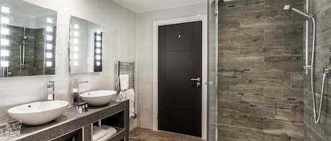 A modern bathroom with a glass-enclosed shower, two sinks, and a dark door.