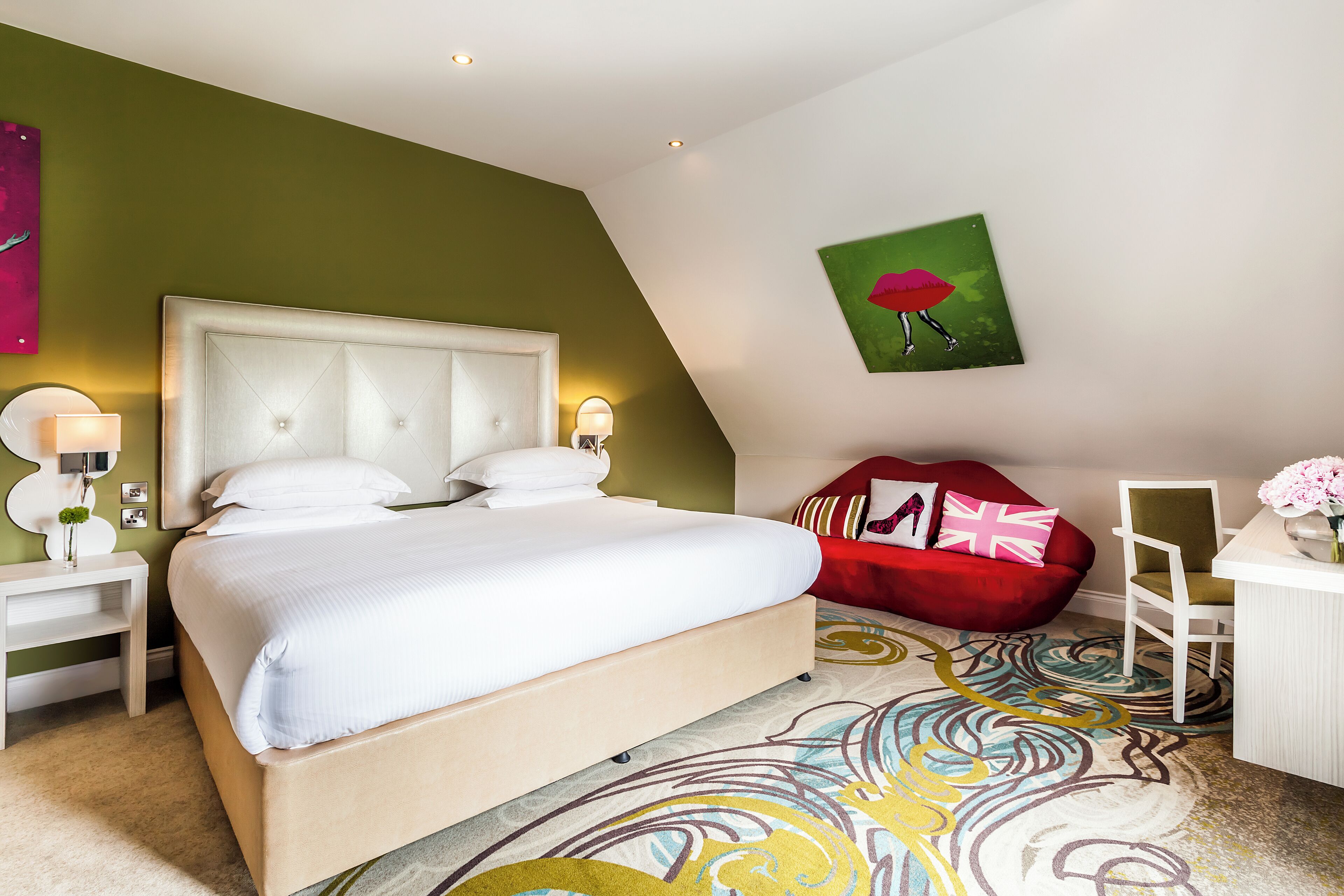 A hotel room with a large bed, a red sofa, a white desk, and a colorful carpet.
