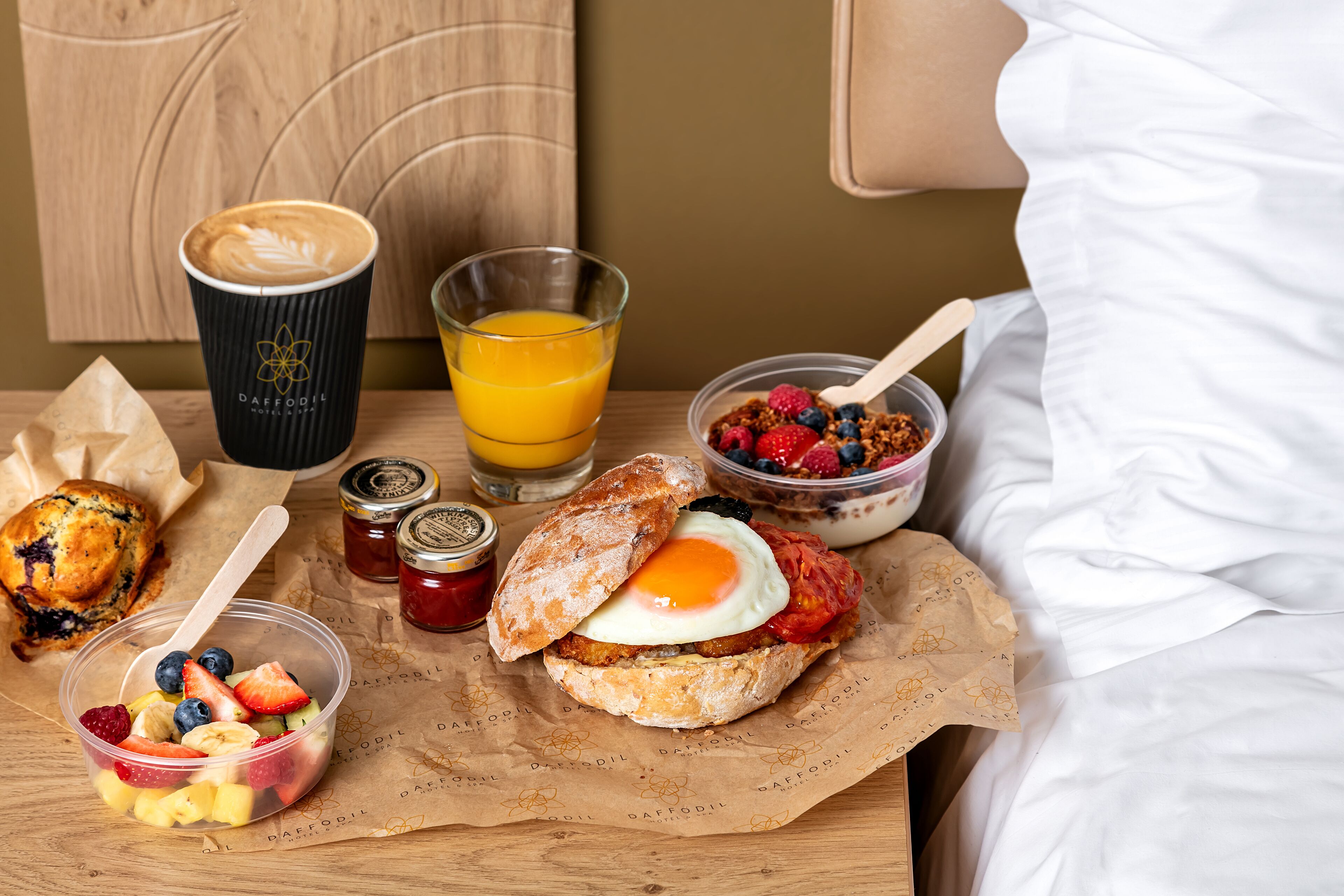 A breakfast tray with a muffin, a cup of coffee, a glass of orange juice, a bowl of cereal with berries, and a sandwich with an egg.